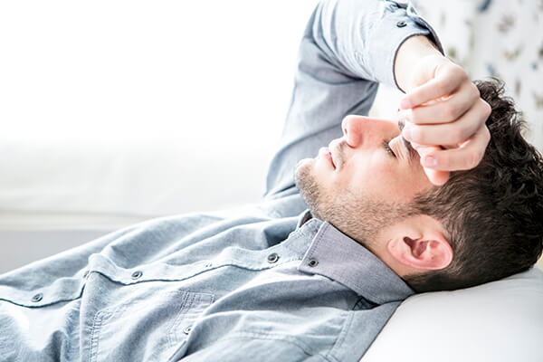 Man lying down and putting hand across forehead